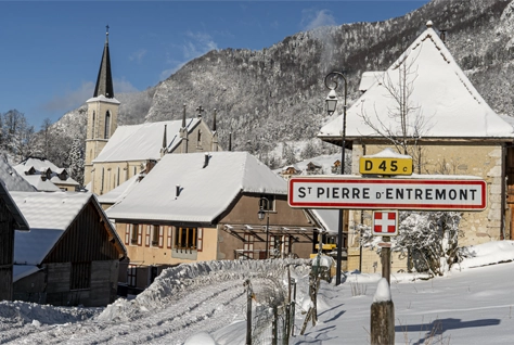 Entrée de Saint-Pierre-d’Entremont en Chartreuse sous la neige avec le gîte Le Passage à l’arrière-plan