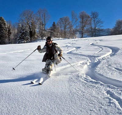 Skieur en ski de randonnée descendant une pente enneigée en Chartreuse sous un ciel bleu
